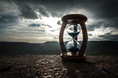 Hourglass Passing Of Time Lapse Clouds. An Hourglass In Front Of A Bright Blue Sky With Puffy White Clouds Passing. Time Concept. Stock Photo Hourglass Passing Of Time Lapse Clouds. An Hourglass In Front Of A Bright Blue Sky With Puffy White Clouds Passing. Time Concept. Stock Photo