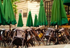 Houten lijsten en stoelen op stadsachtergrond, het concept van de de zomerkoffie met groene paraplu's in openlucht, exemplaarruim royalty-vrije stock foto Houten lijsten en stoelen op stadsachtergrond, het concept van de de zomerkoffie met groene paraplu's in openlucht, exemplaarruim royalty-vrije stock foto