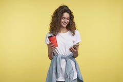 Härlig blyg brunettkvinna som pratar via whatsappbudbärare henne som rymmer kaffekoppen, ett skott som isoleras över guling royaltyfri foto Härlig blyg brunettkvinna som pratar via whatsappbudbärare henne som rymmer kaffekoppen, ett skott som isoleras över guling royaltyfri foto
