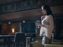 Härlig flickamodell som poserar anseende med ett exponeringsglas av rött vin i hennes hand i en restaurang royaltyfri foto Härlig flickamodell som poserar anseende med ett exponeringsglas av rött vin i hennes hand i en restaurang royaltyfri foto