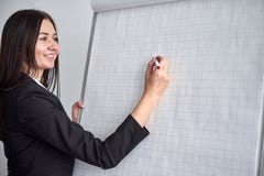 Härlig le handstil för ung kvinna på en tom flipchart i regeringsställning, som hon gör en presentation eller en befordran royaltyfri bild Härlig le handstil för ung kvinna på en tom flipchart i regeringsställning, som hon gör en presentation eller en befordran royaltyfri bild