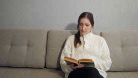 Härlig ung kvinna som hemma sitter på soffan och läseboken lager videofilmer Härlig ung kvinna som hemma sitter på soffan och läseboken lager videofilmer