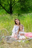 Härlig ung moder och hennes lilla dotter i den vita klänningen som har gyckel i en picknick De sitter på en pläd på gräset och royaltyfria foton Härlig ung moder och hennes lilla dotter i den vita klänningen som har gyckel i en picknick De sitter på en pläd på gräset och royaltyfria foton