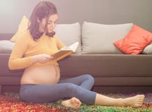 Härligt sunt gravid kvinnasammanträde på mattan och reding arkivfoto Härligt sunt gravid kvinnasammanträde på mattan och reding arkivfoto