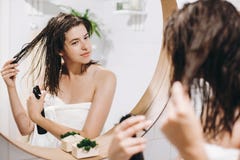 Hår- och kroppomsorg Ung lycklig kvinna i den vita handduken som applicerar hårbalsammaskeringen på hår i badrum, spegelreflexion arkivbild Hår- och kroppomsorg Ung lycklig kvinna i den vita handduken som applicerar hårbalsammaskeringen på hår i badrum, spegelreflexion arkivbild