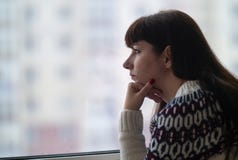 I capelli lunghi della donna guardano meditatamente il primo piano della finestra, contro lo sfondo delle case immagine stock libera da diritti I capelli lunghi della donna guardano meditatamente il primo piano della finestra, contro lo sfondo delle case immagine stock libera da diritti