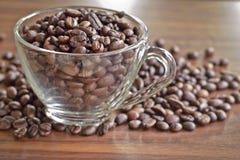 I chicchi di caffè arrostiti in una tazza ed in un mucchio di caffè hanno messo sopra la t di legno immagini stock libere da diritti I chicchi di caffè arrostiti in una tazza ed in un mucchio di caffè hanno messo sopra la t di legno immagini stock libere da diritti