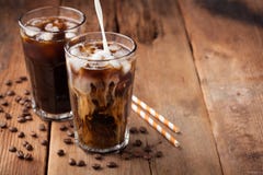 Ice coffee in a tall glass with cream poured over and coffee beans on a old rustic wooden table. Cold summer drink on a dark woode Royalty Free Stock Image Ice coffee in a tall glass with cream poured over and coffee beans on a old rustic wooden table. Cold summer drink on a dark woode Royalty Free Stock Image