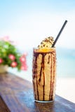 Iced ha mescolato il frappucino del cioccolato e del latte con panna montata sulla spiaggia immagine stock Iced ha mescolato il frappucino del cioccolato e del latte con panna montata sulla spiaggia immagine stock