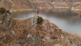 Ideia a?rea de uma posi??o da menina em uma rocha na costa de um lago, que fotografe a paisagem em sua c?mera de DSLR video estoque Ideia a?rea de uma posi??o da menina em uma rocha na costa de um lago, que fotografe a paisagem em sua c?mera de DSLR video estoque