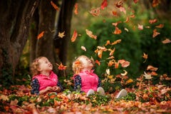 Identical Twins Having Fun With Autumn Leaves In The Park, Blond Cute Curly Girls, Happy Kids, Beautiful Girls In Pink Jackets Stock Photo