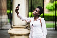 Iklädd moderiktig tillfällig dräkt för attraktiv afro för amerikan som blogger för ung kvinna gör selfie via smartphonen för att royaltyfria bilder Iklädd moderiktig tillfällig dräkt för attraktiv afro för amerikan som blogger för ung kvinna gör selfie via smartphonen för att royaltyfria bilder