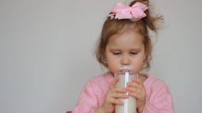 Il bambino beve una bevanda a base di latte - il kefir, i frullati, il cocktail, yogurt Una bambina piacevole che tiene un vetro video d archivio Il bambino beve una bevanda a base di latte - il kefir, i frullati, il cocktail, yogurt Una bambina piacevole che tiene un vetro video d archivio