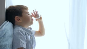 Il bambino felice beve l'acqua da vetro che si siede sulla finestra a casa video d archivio Il bambino felice beve l'acqua da vetro che si siede sulla finestra a casa video d archivio