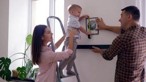 Il bambino grazioso con gli aiuti madre ed il padre della misura di nastro appende lo scaffale con l'immagine sulla parete dopo l video d archivio Il bambino grazioso con gli aiuti madre ed il padre della misura di nastro appende lo scaffale con l'immagine sulla parete dopo l video d archivio