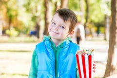 Il bambino sorridente con un secchio di popcorn a disposizione cammina nel parco immagini stock Il bambino sorridente con un secchio di popcorn a disposizione cammina nel parco immagini stock