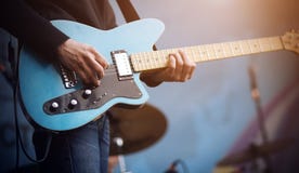 Il chitarrista esegue una melodia su una chitarra elettrica blu immagine stock Il chitarrista esegue una melodia su una chitarra elettrica blu immagine stock