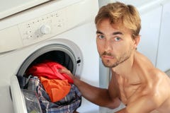 Il giovane bello carica la lavanderia nella lavatrice Casalinga maschio, concetto del celibe immagini stock Il giovane bello carica la lavanderia nella lavatrice Casalinga maschio, concetto del celibe immagini stock