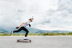 Il giovane Longboarder spinge il suo piede fuori sul suo longboard sopra la strada campestre fotografie stock Il giovane Longboarder spinge il suo piede fuori sul suo longboard sopra la strada campestre fotografie stock