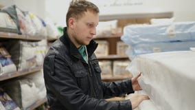 Il giovane sta scegliendo un materasso in un grande negozio o supermercato della mobilia Sta controllando la sua elasticità, schi stock footage Il giovane sta scegliendo un materasso in un grande negozio o supermercato della mobilia Sta controllando la sua elasticità, schi stock footage