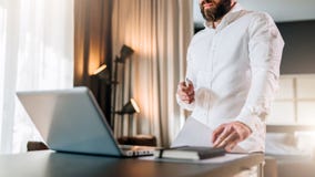 Il giovane uomo d'affari barbuto in camicia bianca è scrittorio vicino diritto davanti al computer portatile, documenti della ten immagine stock libera da diritti Il giovane uomo d'affari barbuto in camicia bianca è scrittorio vicino diritto davanti al computer portatile, documenti della ten immagine stock libera da diritti