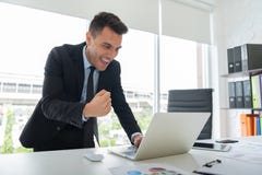 Il giovane uomo d'affari felice è stante ed esaminante il computer portatile fotografia stock libera da diritti Il giovane uomo d'affari felice è stante ed esaminante il computer portatile fotografia stock libera da diritti