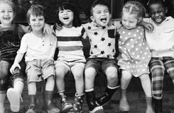 Il gruppo di asilo scherza il braccio degli amici intorno alla seduta e allo smilin immagini stock Il gruppo di asilo scherza il braccio degli amici intorno alla seduta e allo smilin immagini stock