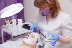 Il padrone mette una maschera bianca con una spazzola sul fronte di una giovane donna che si trova sulla tavola immagini stock Il padrone mette una maschera bianca con una spazzola sul fronte di una giovane donna che si trova sulla tavola immagini stock