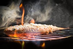 Il pesce sulla griglia/si chiude su del mangime per pesci arrostito dei frutti di mare con sale sul fuoco e sul fumo della grigli immagine stock Il pesce sulla griglia/si chiude su del mangime per pesci arrostito dei frutti di mare con sale sul fuoco e sul fumo della grigli immagine stock