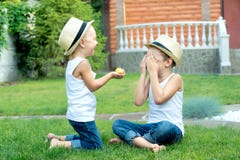 Il ragazzino dà a suo fratello il cereale Due fratelli che si siedono sull'erba e mangiare pannocchia nel giardino immagine stock Il ragazzino dà a suo fratello il cereale Due fratelli che si siedono sull'erba e mangiare pannocchia nel giardino immagine stock