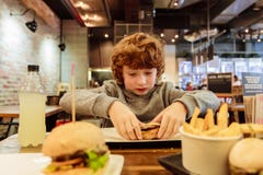 Il ragazzo affamato mangia l'hamburger in ristorante fotografia stock Il ragazzo affamato mangia l'hamburger in ristorante fotografia stock