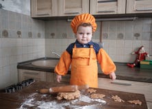 Il ragazzo europeo sveglio in un vestito del cuoco produce i biscotti dello zenzero immagine stock Il ragazzo europeo sveglio in un vestito del cuoco produce i biscotti dello zenzero immagine stock