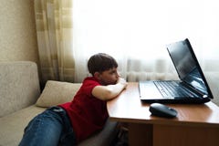 Il ragazzo si trova nel salone sullo strato e guarda un film su un computer portatile fotografia stock libera da diritti Il ragazzo si trova nel salone sullo strato e guarda un film su un computer portatile fotografia stock libera da diritti