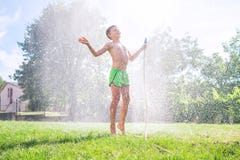 Il ragazzo sveglio del bambino in età prescolare si rinfresca dal tubo flessibile d'innaffiatura del giardino sull'iarda dell'erb fotografia stock Il ragazzo sveglio del bambino in età prescolare si rinfresca dal tubo flessibile d'innaffiatura del giardino sull'iarda dell'erb fotografia stock