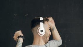 Il ritratto del primo piano di giovane uomo divertente mette sopra le cuffie ed il dancing pazzo mentre ascolti musica su fondo n stock footage Il ritratto del primo piano di giovane uomo divertente mette sopra le cuffie ed il dancing pazzo mentre ascolti musica su fondo n stock footage