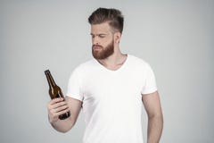 Il ritratto di bello uomo barbuto sexy vestito in una maglietta bianca tiene una bottiglia della birra in sua mano sta dentro fotografia stock Il ritratto di bello uomo barbuto sexy vestito in una maglietta bianca tiene una bottiglia della birra in sua mano sta dentro fotografia stock