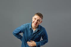 Il tipo di risata vestito in una camicia dei jeans tiene la sua mano sullo stomaco nello studio sui precedenti grigi immagine stock libera da diritti Il tipo di risata vestito in una camicia dei jeans tiene la sua mano sullo stomaco nello studio sui precedenti grigi immagine stock libera da diritti