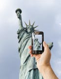 Il turista sostiene il telefono della macchina fotografica alla statua della libertà fotografia stock Il turista sostiene il telefono della macchina fotografica alla statua della libertà fotografia stock