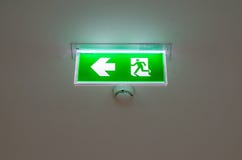 Illuminated green exit sign suspended from the ceiling Stock Photos Illuminated green exit sign suspended from the ceiling Stock Photos