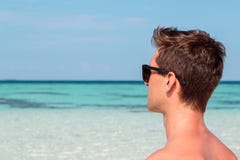 Image de trois-quarts d'un jeune homme sur la plage regardant la mer bleue claire photos libres de droits Image de trois-quarts d'un jeune homme sur la plage regardant la mer bleue claire photos libres de droits
