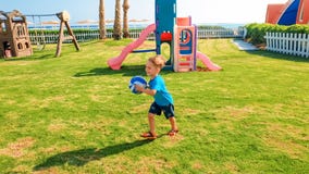Image du gar?on gai riant heureux tenant la boule du football dans les mains et le fonctionnement sur le terrain de jeu d'enfants photographie stock libre de droits Image du gar?on gai riant heureux tenant la boule du football dans les mains et le fonctionnement sur le terrain de jeu d'enfants photographie stock libre de droits