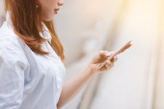 Imagem colhida da mulher asiática nova atrativa que guarda o telefone esperto móvel na rua da cidade com efeito da luz do sol soc fotografia de stock Imagem colhida da mulher asiática nova atrativa que guarda o telefone esperto móvel na rua da cidade com efeito da luz do sol soc fotografia de stock