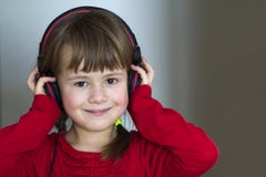 Imagem da menina bonita feliz da criança com fones de ouvido grandes em casa A menina alegre da criança que escuta a música no ci imagem de stock Imagem da menina bonita feliz da criança com fones de ouvido grandes em casa A menina alegre da criança que escuta a música no ci imagem de stock