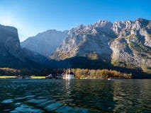 Imagem do Koenigssee com a capela de St Bartholomew e de um barco de turista No fundo a formação iluminada da montanha fotografia de stock Imagem do Koenigssee com a capela de St Bartholomew e de um barco de turista No fundo a formação iluminada da montanha fotografia de stock