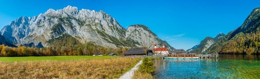 Imagem do panorama do Koenigssee com a capela de St Bartholomew e de um barco de turista No fundo a montanha iluminada fotos de stock royalty free Imagem do panorama do Koenigssee com a capela de St Bartholomew e de um barco de turista No fundo a montanha iluminada fotos de stock royalty free