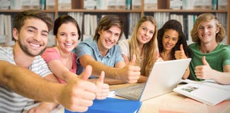 Imagen compuesta de los estudiantes universitarios que gesticulan los pulgares para arriba en biblioteca imagen de archivo libre de regalías Imagen compuesta de los estudiantes universitarios que gesticulan los pulgares para arriba en biblioteca imagen de archivo libre de regalías