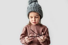 Imagen de la niña linda que juega en el sombrero caliente del invierno, suéter que lleva con las gafas elegantes redondas en un e foto de archivo libre de regalías Imagen de la niña linda que juega en el sombrero caliente del invierno, suéter que lleva con las gafas elegantes redondas en un e foto de archivo libre de regalías