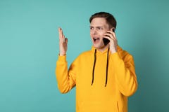Imagen del hombre de griterío joven en la situación de la sudadera con capucha del yellowe aislado sobre fondo azul de la pared imagen de archivo libre de regalías Imagen del hombre de griterío joven en la situación de la sudadera con capucha del yellowe aislado sobre fondo azul de la pared imagen de archivo libre de regalías