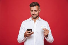 Immagine dell'uomo felice nella carta di credito della tenuta della camicia e nello smartp bianchi immagini stock libere da diritti Immagine dell'uomo felice nella carta di credito della tenuta della camicia e nello smartp bianchi immagini stock libere da diritti