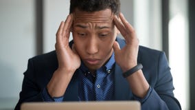 Impiegato afroamericano stanco che soffre dall'emicrania facendo uso del computer portatile fotografia stock libera da diritti Impiegato afroamericano stanco che soffre dall'emicrania facendo uso del computer portatile fotografia stock libera da diritti